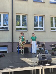Dyrektor szkoły wraz z prowadzącą stoją na scenie i witają gości.